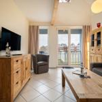 Wohnzimmer mit Holzmöbeln, Fernseher und Balkonansicht.