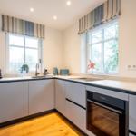 Moderne Küche mit zwei Fenstern, grauen Schränken und integriertem Backofen.