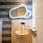 Bad mit Steinwaschbecken, Wandspiegel und Holzwandverkleidung.