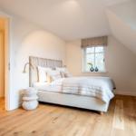 Schlafzimmer mit Bett, Fenster und angrenzender Badewanne.