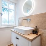 Badezimmer mit Waschbecken, Spiegel und Fenster. Holzoberfläche und Steinwand.