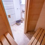 Sauna mit Holzbänken und Blick in das Badezimmer mit Dusche.