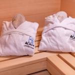 Zwei weiße Bademäntel mit Logo liegen auf Holzbank in Sauna.