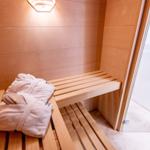 Sauna mit Holzbank und Bademantel. Tür führt in Duschbereich.