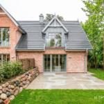 Modernes Haus mit Steinmauer und großem Garten. Große Fenster und Terrasse.