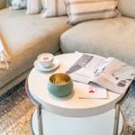 Runde Tisch mit Kaffeetasse, Zeitschrift und Schale vor einem Sofa.