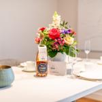 Tisch gedeckt mit Blumen, Wein und Geschirr.