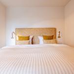 Ein Bett mit weißer Bettdecke und gelben Kissen. An den Wänden hängen Wandlampen.