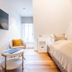 Schlafzimmer mit Bett, Nachttisch, Sessel und Fernseher an der Wand.