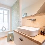 Badezimmer mit Waschbecken, Spiegel und Fenster. Holzoberfläche und Wandverkleidung.