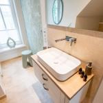 Bad mit Waschtisch, Spiegel und Fenster. Holzoberfläche und Wandfliesen.