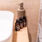 Badewanne mit Seifenspender und kleinen Flaschen auf Holzunterlage.