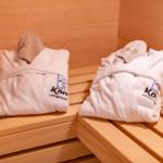 Zwei weiße Bademäntel mit Mützen liegen auf Holzbänken in einer Sauna.