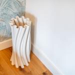 Weißer, wellenförmiger Vasenständer an der Wand mit gemustertem Tapetenabschnitt.