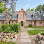 Ein Backsteinhaus mit grauem Dach und gepflastertem Weg durch einen grünen Garten.