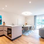 Moderne Küche mit Essbereich und Sitzgelegenheit. Große Fenster mit Blick auf Garten.