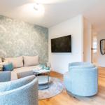 Wohnzimmer mit Sofa, zwei Sesseln und Wandbild. Fernseher an der Wand.