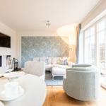 Wohn- und Essbereich mit Sofa, runden Sessel und großem Fenster. Wand mit Muster. Esstisch mit Geschirr.