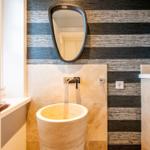 Bad mit Steinspüle, Wandspiegel und gestreifter Tapete.