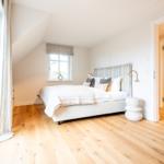 Schlafzimmer mit Dachschrägen, Holzboden und Blick in das Bad.