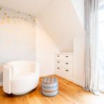 Zimmer mit weißer Sitzgelegenheit, Holzboden und großem Fenster.