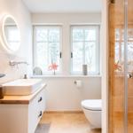 Badezimmer mit Dusche, Waschbecken und Toilette. Fenster mit Blick auf Bäume.