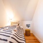 Schlafzimmer mit Bett, Nachttisch und Stuhl unter schrägen Wänden.