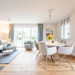 Wohn- und Essbereich mit Sofa, Tisch und Stühlen sowie Fenstern.