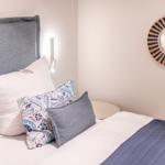 Ein Bett mit Kissen und einer Decke, Wandspiegel und Nachttisch