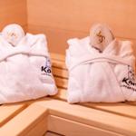 Zwei weiße Bademäntel mit Schuhen liegen auf Holzbank in Sauna.