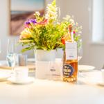 Tisch mit Blumen, Gläsern und einer Flasche Willkommensgetränk.