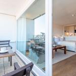 Terrasse mit Tisch und Stühlen. Wohn- und Schlafbereich mit Holzboden und Glaswand.