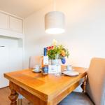 Esstisch mit Stühlen, Blumen und Flasche. Hintergrund: weiße Schränke und Deckenleuchte.