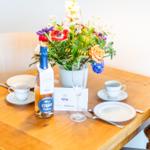 Holztisch mit Blumenvase, Gläsern und Tassen für zwei Personen.