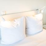 Ein Bett mit weißen Kissen und Nachttisch mit Blumen.