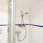 Dusche mit Duschbrause und blauer Zierleiste an den Wänden.