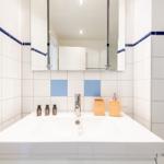 Bad mit weißen Fliesen und blauen Akzenten, Waschbecken und Spiegel.