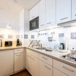 Küche mit weißen Schränken, Spüle, Herd und Kühlschrank.