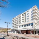 Hotelgebäude mit Balkonen und Eingangsbereich an sonnigem Tag.