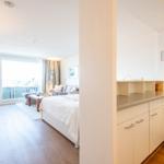 Wohnung mit Küche, Schlafzimmer und Balkon. Holzfußboden und weiße Möbel.