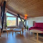 Wohnzimmer mit rotem Sofa, zwei Sesseln und großen Fenstern. Holzdecke und Boden.