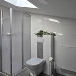 Badezimmer mit Dusche, Waschbecken und Toilette. Weiße Fliesen und Pflanzen.