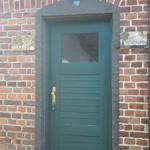 Grüne Haustür mit Glasfenster in rotem Ziegelhaus. Schilder an der Wand.