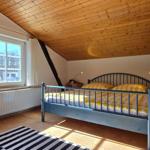 Schlafzimmer mit Holzdecke, Bett mit gelbem Bettbezug und zwei Fenstern.