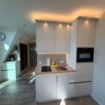 Moderne Küche mit eingebauter Spüle und Backofen. Helle Holzdielen und weiße Schränke.