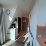 Flur mit Küchenzeile, Kaffeemaschine und Wanduhr. Holzfußboden und Fenster mit Vorhang.