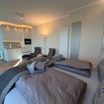 Zwei Betten mit Bettwäsche, Küchenbereich und zwei Sessel im Raum.