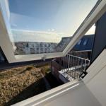 Durch das geöffnete Fenster ist die Aussicht auf Gebäude und Grünflächen zu sehen.