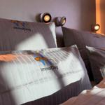 Bettkopfteil mit Kissen und Wandlampen. Kissen mit Logo.