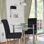 Esstisch mit zwei Stühlen, Glasplatte, vor Fenster mit Blick auf Balkon.